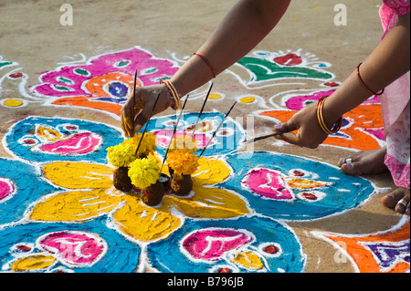 Indische Frau Inverkehrbringen Räucherstäbchen in ein Angebot von Blumen und Kuhmist auf einem Rangoli Design an Sankranti in einem indischen Straße. Andhra Pradesh, Indien Stockfoto