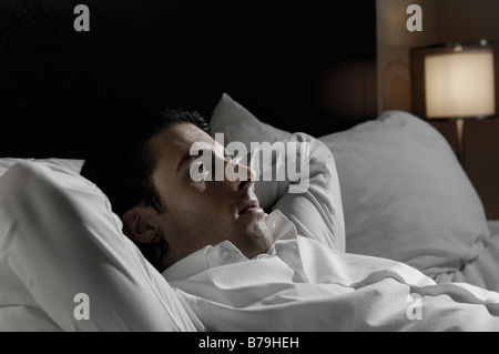 Junger Mann allein im Bett liegend Stockfoto