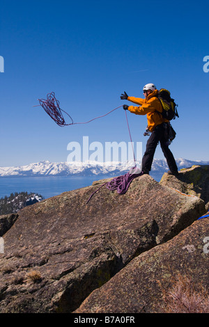 Ein Bergsteiger wirft ein Seil von einer Klippe über dem Lake Tahoe und die schneebedeckten Berge der Sierra Nevada Stockfoto