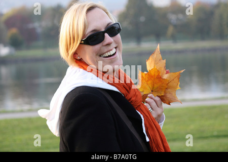 Frau trägt Sonnenbrille und hält herbstliche Blätter Stockfoto