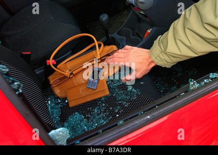 Auto-Einbruch, Hand greift durch das Seitenfenster an Wertsachen, d.h. Handtasche, Geldbörse und Handy Stockfoto