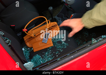 Auto-Einbruch, Hand greift durch das Seitenfenster an Wertsachen, d.h. Handtasche, Geldbörse und Handy Stockfoto