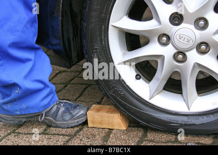 Holzblock eingekeilt auf Pkw-Reifen, Auto Rollen zu verhindern Stockfoto