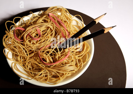 Gummibänder vorgeben, Nudeln in Schüssel mit schwarzen Bleistift Stäbchen auf braun Tischset auf weißen Tisch zu sein. Stockfoto