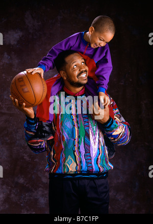 Ein afrikanischer amerikanischer Vater gibt seinem Sohn eine Huckepack Reiten mit einem Basketball Herr Stockfoto