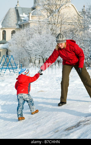 Glückliche Familie Mutter mit kleinen Jungen im Winterschnee bedeckte Hof in der Nähe von Haus Stockfoto