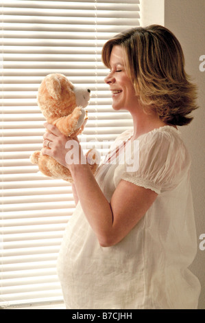 Schwangere Frau durch Fenster blickte auf Teddybär, Kinderspielzeug stehen. Stockfoto