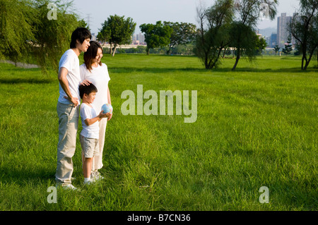 Junge Familie mit einem Kind auf dem Rasen stehen und wegsehen Stockfoto