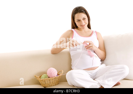 Schwangere Frau stricken mit Wollknäuel sitzen auf dem Sofa zu Lächeln Stockfoto