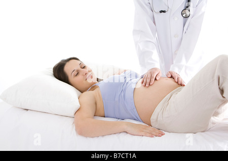 Arzt überprüfen Bauch der eine junge schwangere Frau liegend auf den Rücken Augen geschlossen Stockfoto