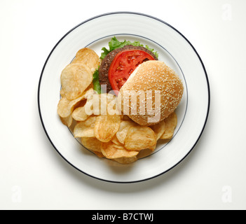 Ein Hamburger mit Salat und Tomate Scheibe mit Kartoffel-Chips auf einem runden weißen Teller serviert. Stockfoto