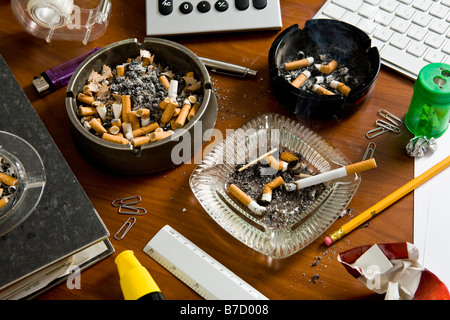 Ein Schreibtisch überladen mit Büromaterial und Aschenbecher Stockfoto