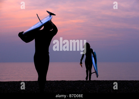 Surfer tragen ihre Boards an den Strand und fangen den letzten Winter Tageslicht aus Brighton in East Sussex. Bild von Jim Holden Stockfoto