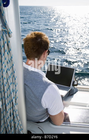 Rückansicht eines Mannes mit einem Laptop auf einer yacht Stockfoto