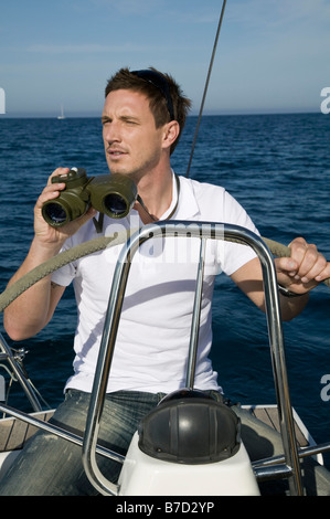 Ein Mann mit dem Fernglas an der Spitze einer Yacht Stockfoto