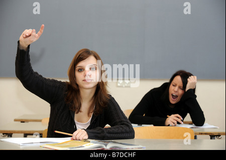 Schulmädchen, indem Sie ihre hand in der Klasse, während eine andere eine fast einschlafen Stockfoto