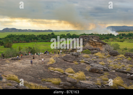 Touristen zu Fuß über die Felsen des Ubirr mit einem Feuer im Hintergrund im Kakadu National Park Stockfoto