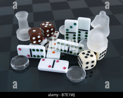 Mattiertes Glas Schach Stücke Dominos Würfel und Steinen angeordnet auf einem mattierten Checker board Stockfoto