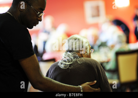 Eine ältere Dame Sikh wird an ihren Stuhl in eine multikulturelle zusätzliche Pflege nach Hause Bradford West Yorkshire geholfen. Stockfoto