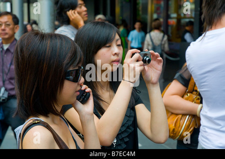 Zwei junge asiatische Mädchen mit Hilfe moderner Technologie in Form von einem Mobiltelefon und einer Digitalkamera Stockfoto