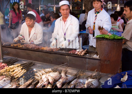 Spieße mit Fisch, Gemüse und Fleisch gegrillt auf Holzkohle bei Nacht-Food-Markt in Urumqi Xinjiang Chinas Hauptstadt Stockfoto