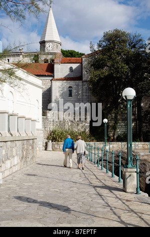 Älterer Mann und Frau zu Fuß entlang der Strandpromenade in Richtung Kirche in Opatija, Kroatien Stockfoto