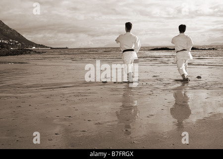 Junge Erwachsene Männer mit schwarzen Gürtel üben eine Kata am Strand an einem sonnigen Tag Stockfoto