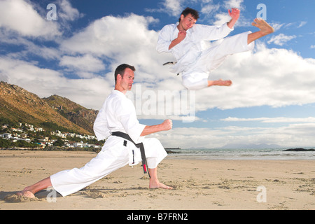 Junge Erwachsene Männer mit schwarzen Gürtel üben eine Kata am Strand an einem sonnigen Tag Stockfoto