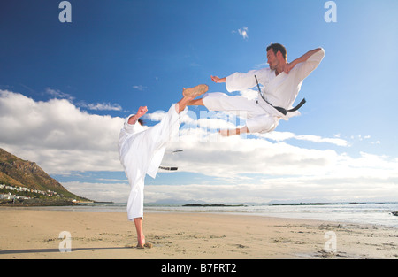 Junge Erwachsene Männer üben Karate am Strand ist man in einem high Kick und die andere etwas Bewegung durch die Luft fliegen Stockfoto