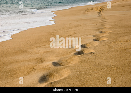 Fußspuren im Sand am Rand des Wassers, die teilweise von Wellen erfasst worden. Stockfoto