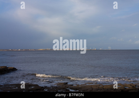 Brandung brechen über Felsen am Seaton Schleuse mit Blyth Strand und Surfer im Hintergrund Stockfoto