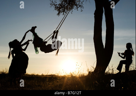 Silhouette der indischen Mädchen Schwingen auf einem hausgemachten Schwingen in den ländlichen indischen Landschaft bei Sonnenuntergang. Andhra Pradesh, Indien Stockfoto