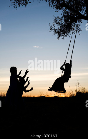 Silhouette der indischen Mädchen Schwingen auf einem hausgemachten Schwingen in den ländlichen indischen Landschaft bei Sonnenuntergang. Andhra Pradesh, Indien Stockfoto