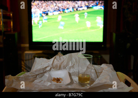 bleibt eine Mahlzeit zum Mitnehmen für eine und Glas Bier auf einem Tablett vor Fußballspiel auf dem tv im Wohnzimmer eines Hauses Stockfoto