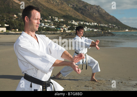 Junge Erwachsene Männer mit schwarzen Gürtel üben eine Kata am Strand an einem sonnigen Tag Stockfoto