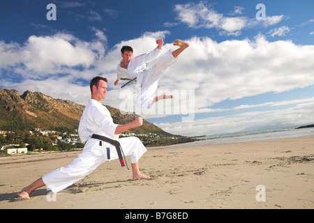 Junge Erwachsene Männer mit schwarzen Gürtel üben eine Kata am Strand an einem sonnigen Tag Stockfoto