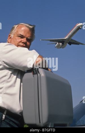 Ältere Mann lehnt sich auf Koffer als Jet fliegen overhead Stockfoto