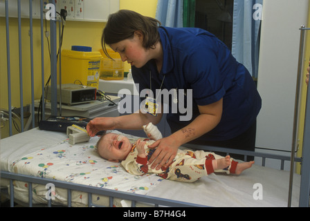 Schwester beruhigt ein weinendes kleines Baby im Krankenhaus, das sich über sein Bett beugt Stockfoto