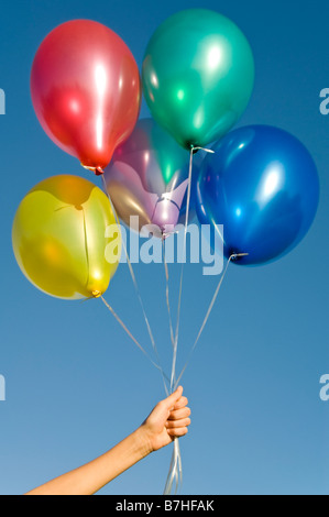 Vertikal nah gefüllt von einer Hand hält eine Reihe von bunten Helium Latexballons vor blauem Himmel Stockfoto