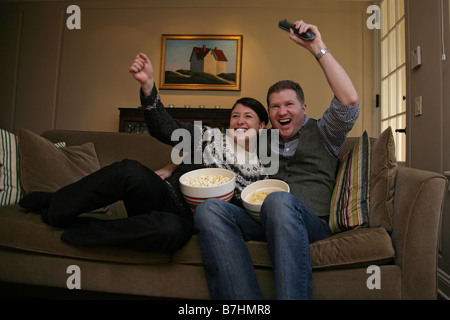 Ein paar wird angeregt durch die Beobachtung ein Sportspiel auf TV zu Hause auf ihrem Sofa im Wohnzimmer. Stockfoto