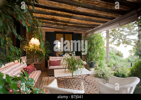 Bequemen Sofas und weißen Lloyd Loom Stühle Oin Wohnzimmer im Freien auf rustikalen Veranda mit üppigen Pflanzen und gemusterten Teppich Stockfoto