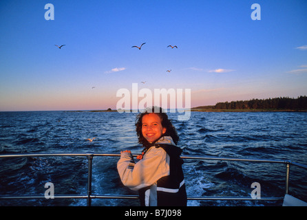 Mädchen, 10, lächelt auf Boot mit Sonnenuntergang und Möwen hinter Nova Scotia Stockfoto