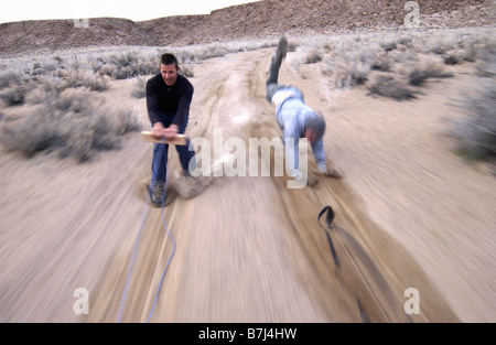 Zwei Männer (20-30) Surfen hinter einem Auto auf einem Feldweg, Bischof, Kalifornien, USA Stockfoto