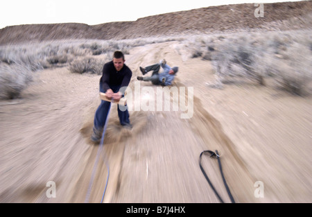 Zwei Männer (20-30) Surfen hinter einem Auto auf einem Feldweg, Bischof, Kalifornien, USA Stockfoto