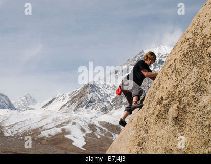 Mann (20-25) Klettern eine Felswand mit einem schneebedeckten Berg im Hintergrund, Bischof, Kalifornien, USA Stockfoto