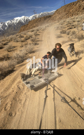 Zwei Männer (20-30) Surfen hinter einem Auto auf einer Kunststoff Palette auf einem Feldweg, Bischof, Kalifornien, USA Stockfoto