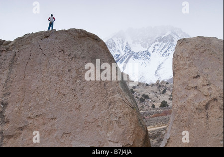 Mann (20-25) Stand auf einem großen Felsbrocken mit einem schneebedeckten Berg in der Ferne Bischof, Kalifornien, USA Stockfoto