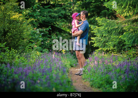 Vater hält Tochter in Armen, küssen, im Wald mit Lupin Blumen, Whistler, BC Stockfoto