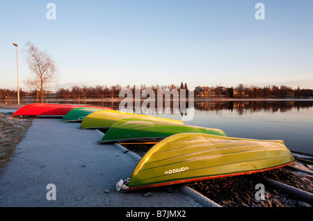 Umgedrehte rote und grüne Fiberglas Ruderboote / Skiffs / Schlauchboote befahren und gelagert am Flussufer, Oulujoki Finnland Stockfoto