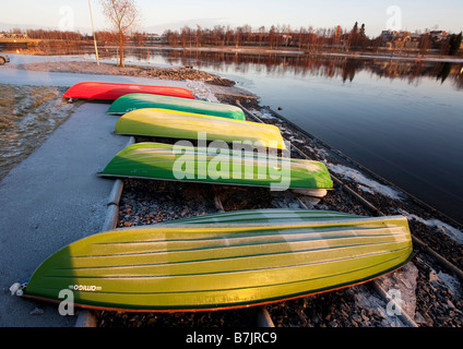 Umgedrehte rote und grüne Fiberglas Ruderboote / Skiffs / Schlauchboote befahren und gelagert am Flussufer, Oulujoki Finnland Stockfoto